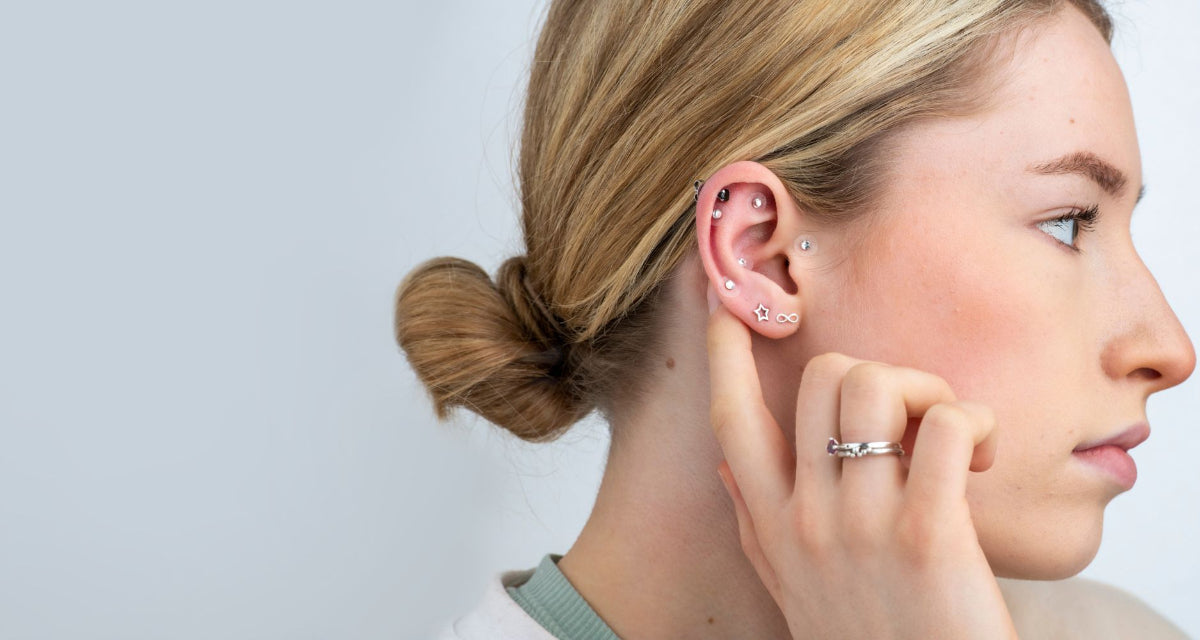 Woman wearing multiple earrings and a ring on a plain background