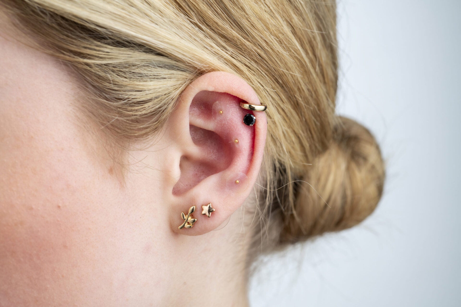 Close-up of an ear with gold earrings and acu seeds on a plain background.