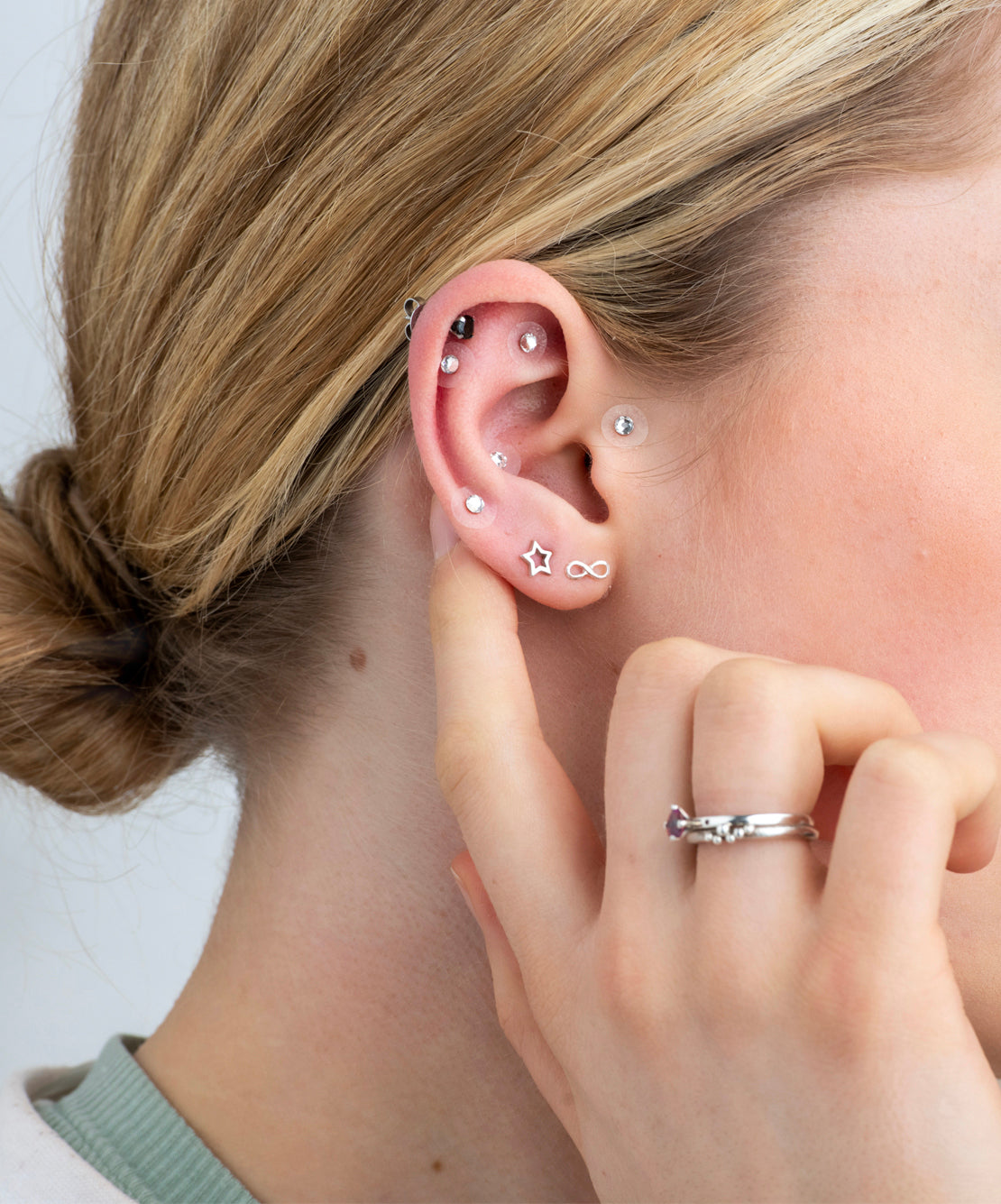 Close-up of a person's ear with multiple earrings and a hand touching the ear.